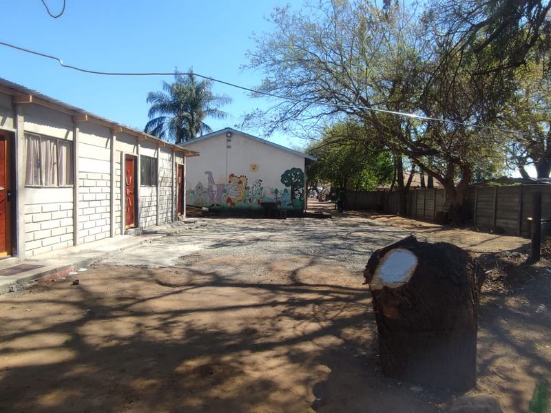 A view of the rear exterior area featuring a concrete block building with timber doors and a large unpaved yard space.