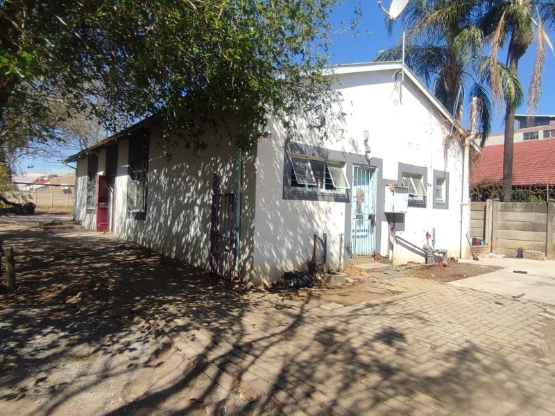 Rear exterior view of the property featuring a paved driveway, precast boundary wall, and basic building structure showing signs of wear.