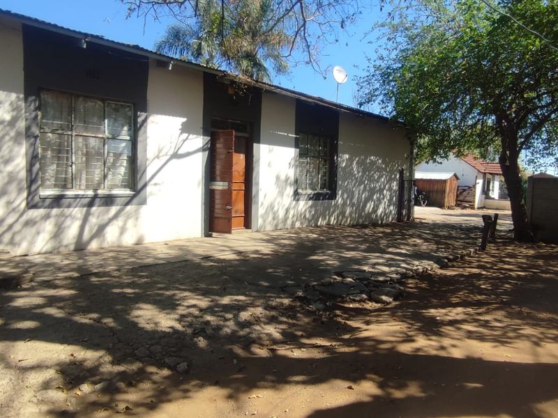 Rear exterior view of the house featuring a concrete patio area, metal window frames, and a perimeter wall in a garden setting.