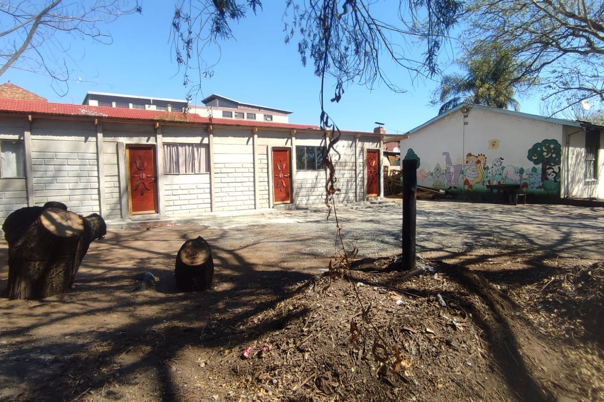 Rear exterior view of a single-story building featuring concrete block construction, multiple entry doors, and a large unpaved yard area.