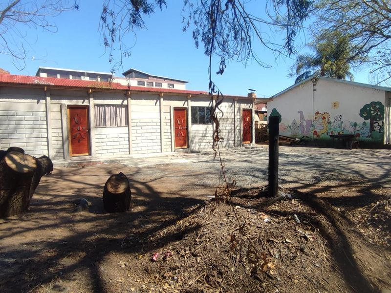 Rear exterior view of a single-story building featuring concrete block construction, multiple entry doors, and a large unpaved yard area.