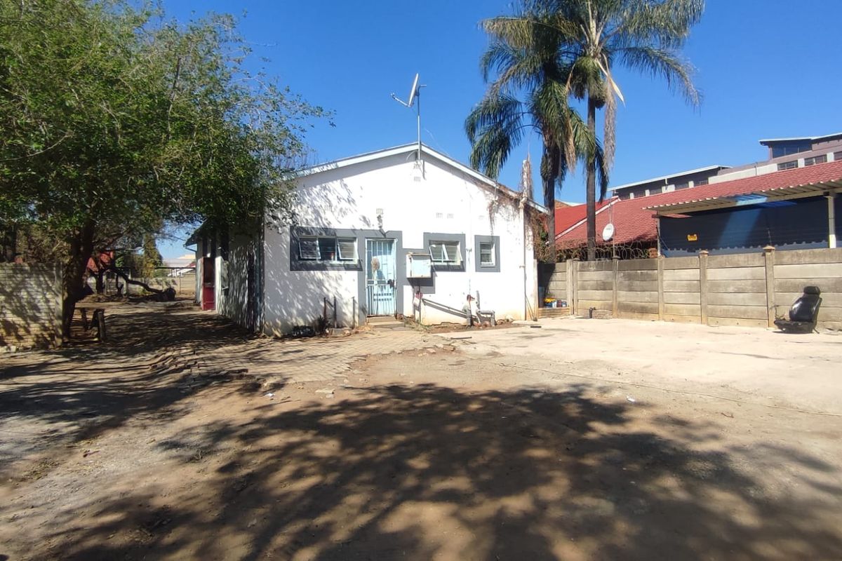 Rear exterior view of the property featuring a concrete driveway, precast boundary wall, and basic building structure requiring maintenance.