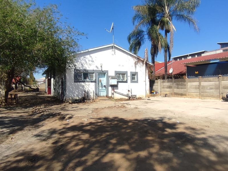 Rear exterior view of the property featuring a concrete driveway, precast boundary wall, and basic building structure requiring maintenance.