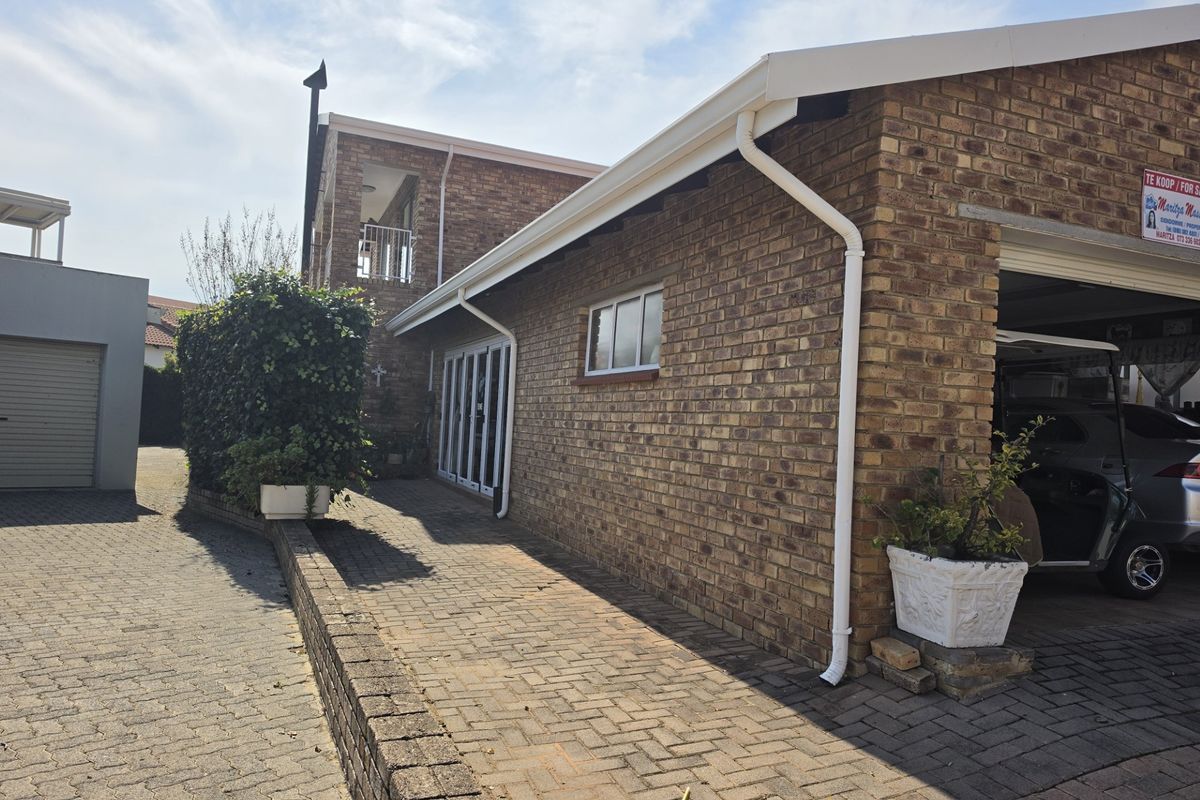 A view of the rear exterior featuring face brick walls, a paved driveway, and access to the garage and sliding glass doors.
