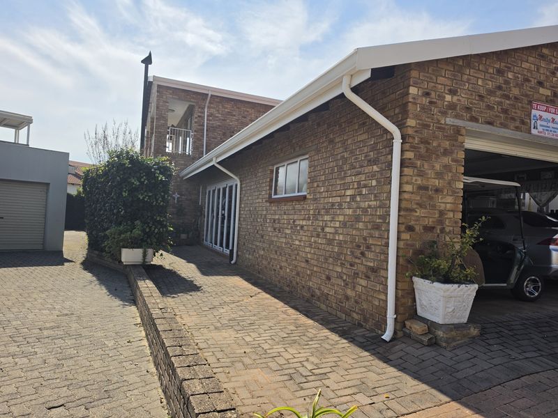 A view of the rear exterior featuring face brick walls, a paved driveway, and access to the garage and sliding glass doors.