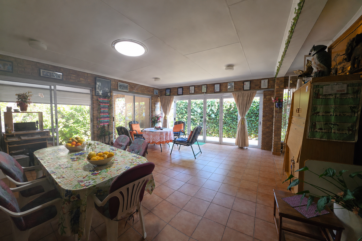 Spacious living area featuring exposed brick walls, tiled flooring, and multiple sliding glass doors providing ample natural light and garden access.