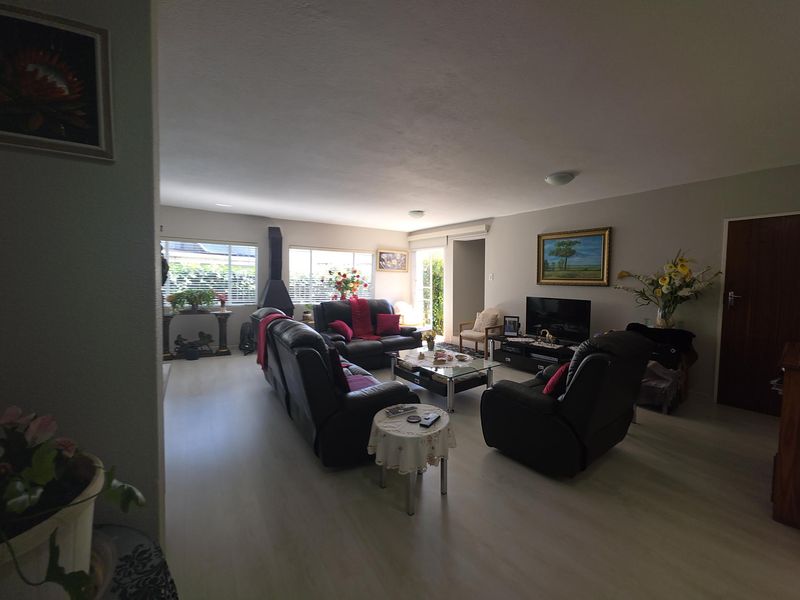 Spacious living room featuring light-toned laminate flooring, a freestanding fireplace, and large windows providing natural light.
