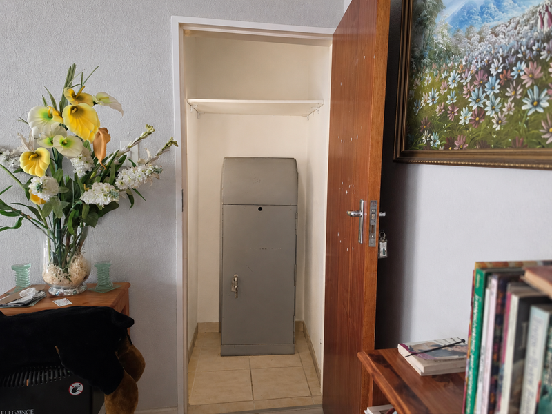 A small utility closet featuring tiled flooring and built-in shelving, currently housing a metal storage unit.