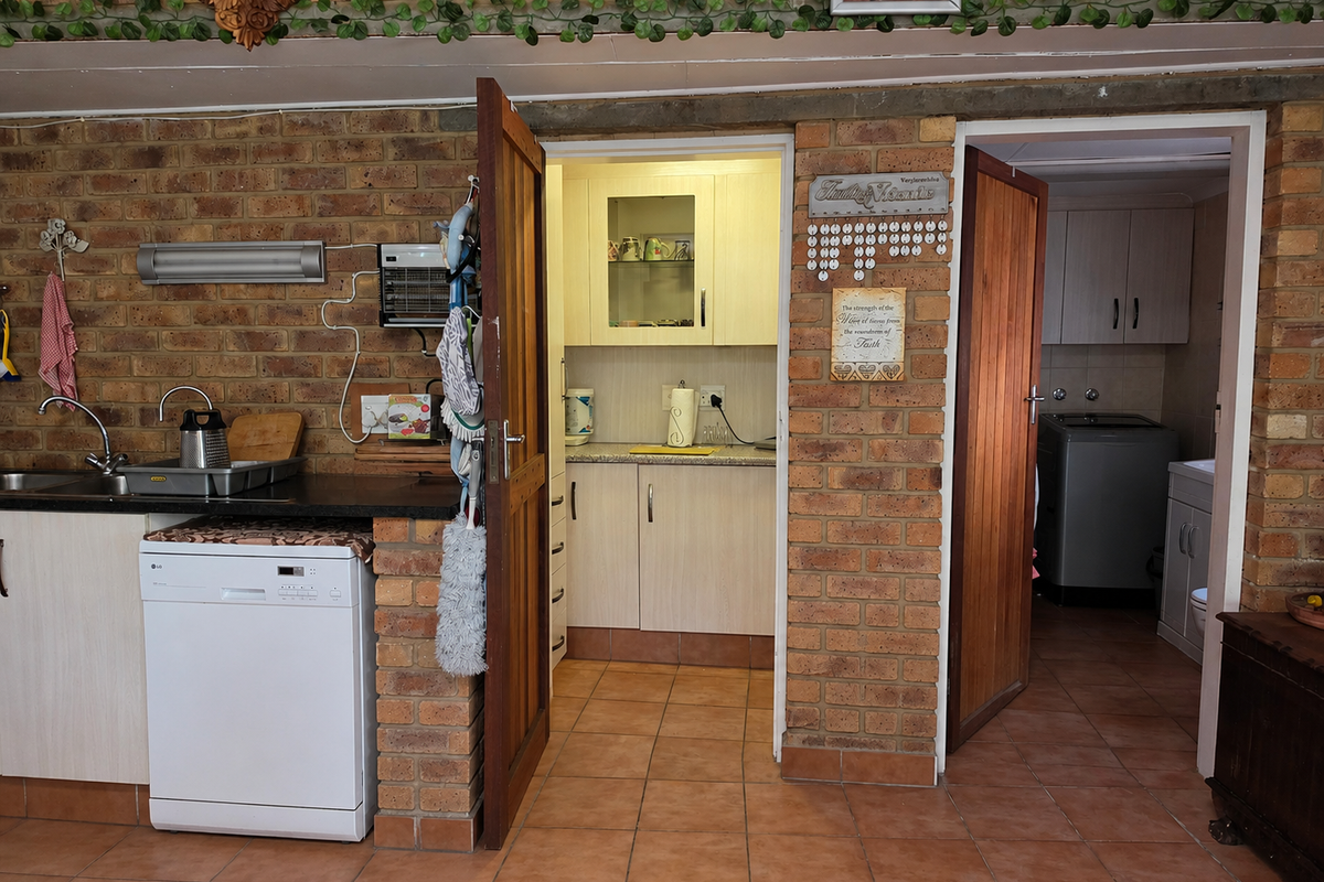 A rustic kitchen featuring exposed brick walls, tiled flooring, and functional built-in cabinetry with an integrated dishwasher and secondary scullery area.