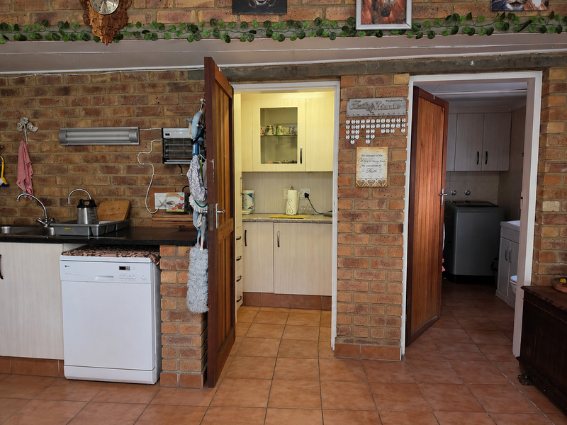A rustic kitchen featuring exposed brick walls, tiled flooring, and functional built-in cabinetry with an integrated dishwasher and secondary scullery area.