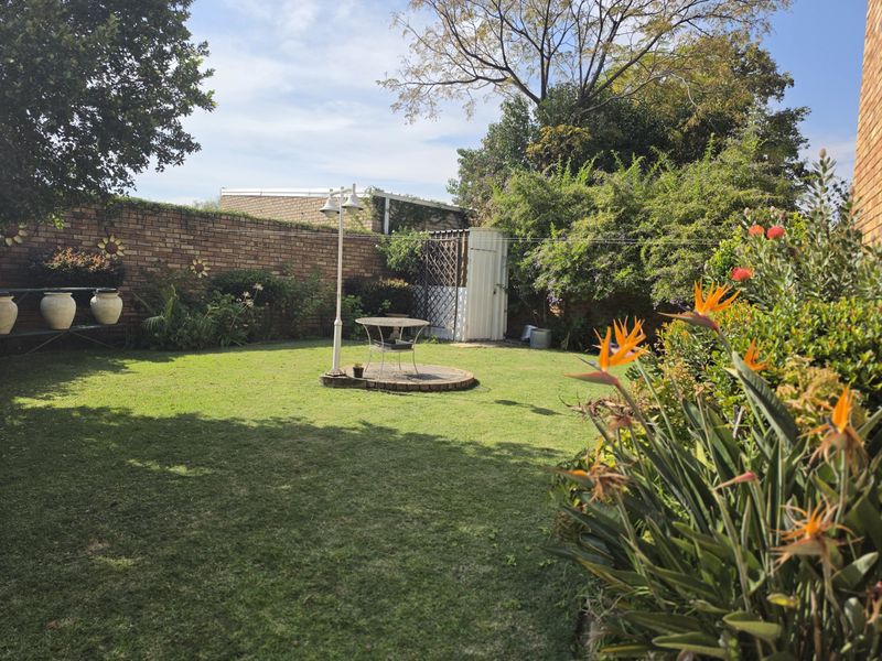A private rear garden featuring a well-maintained lawn, established perimeter brick wall, a paved circular seating area, and a storage shed.