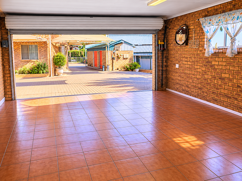 Spacious, clean garage featuring durable tiled flooring and exposed brick walls, with a wide roller door opening to a paved driveway area.
