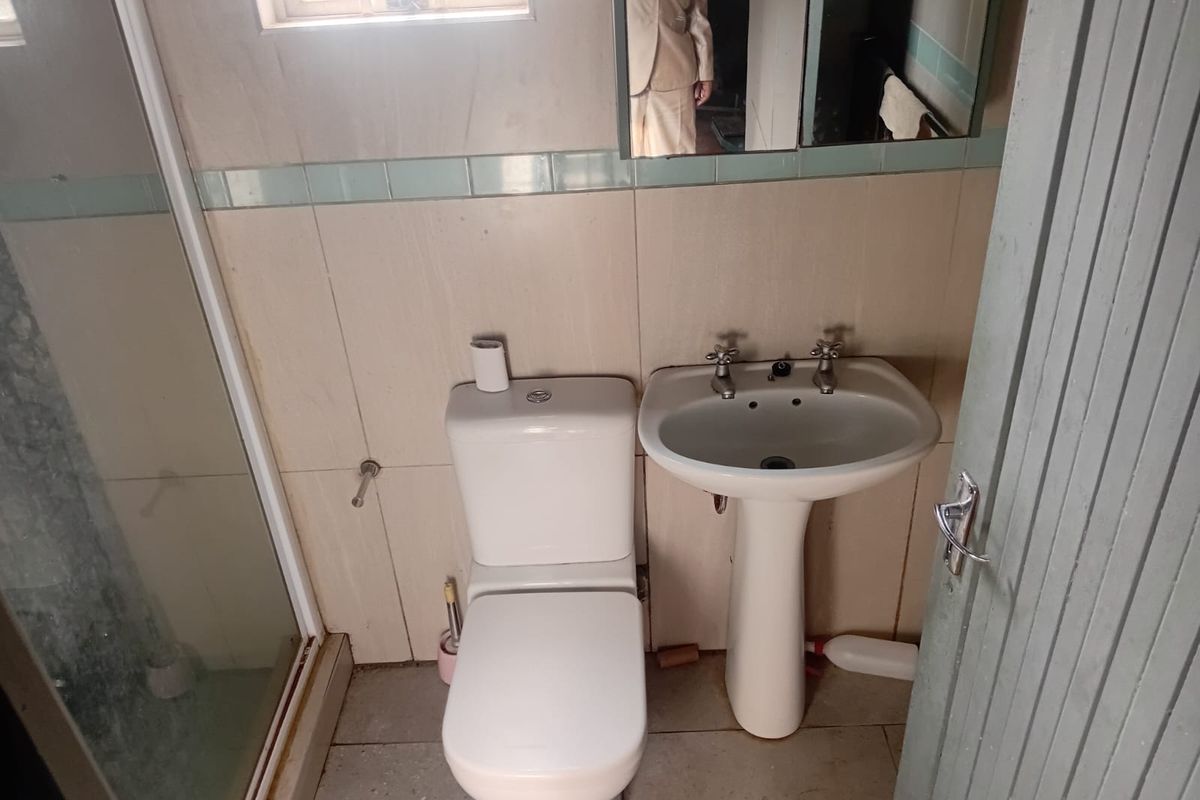 A compact bathroom featuring a pedestal basin, dual flush toilet, and a shower enclosure with tiled walls and flooring.