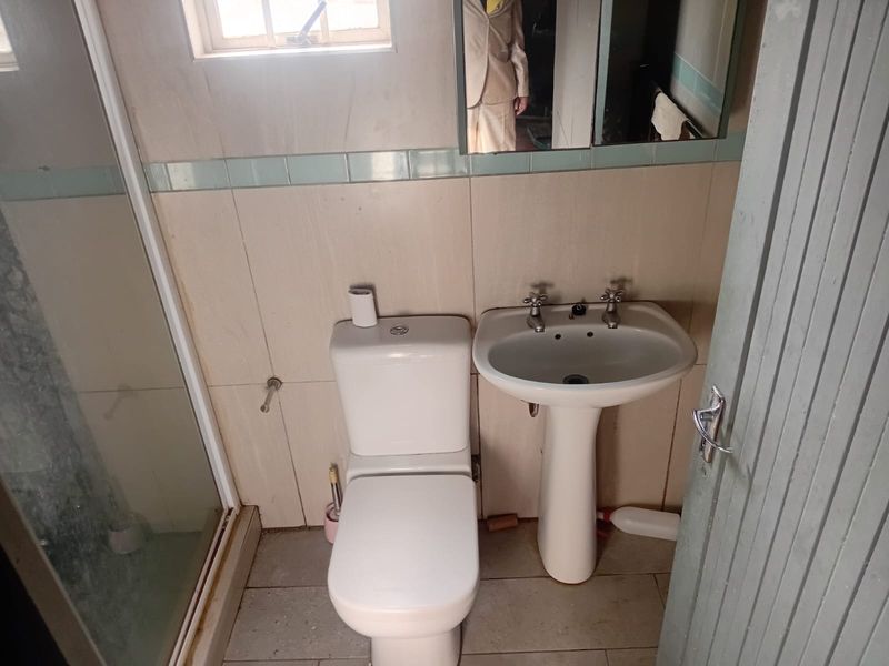 A compact bathroom featuring a pedestal basin, dual flush toilet, and a shower enclosure with tiled walls and flooring.