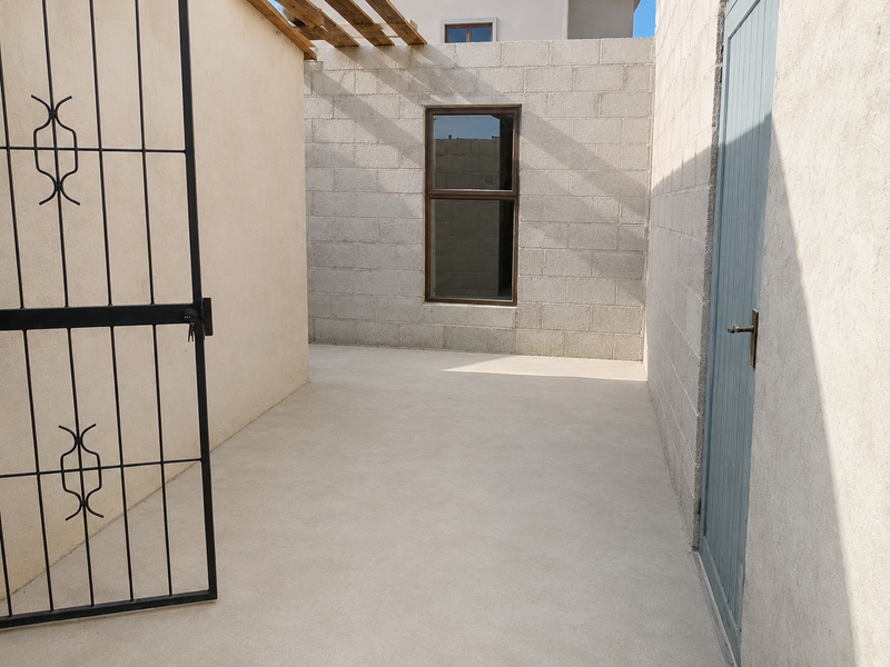 A clean, minimalist outdoor patio area featuring concrete block walls, a timber pergola structure, and secure metal gate access.