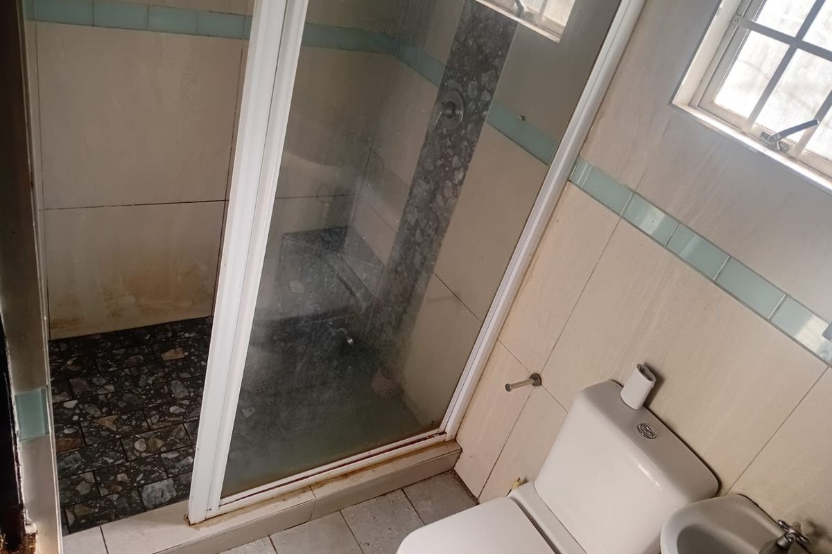 A functional bathroom featuring a shower enclosure, toilet, and basin, with tiled finishes throughout. The space would benefit from cosmetic updates and modernization.