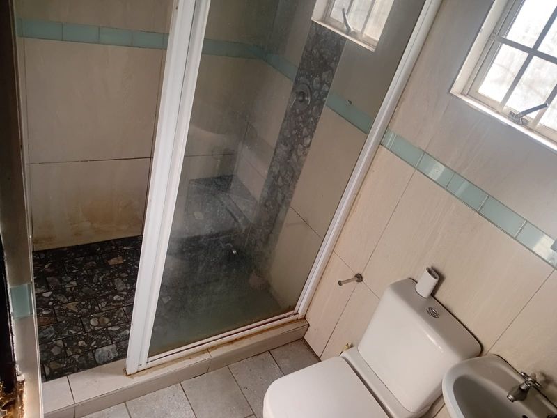 A functional bathroom featuring a shower enclosure, toilet, and basin, with tiled finishes throughout. The space would benefit from cosmetic updates and modernization.