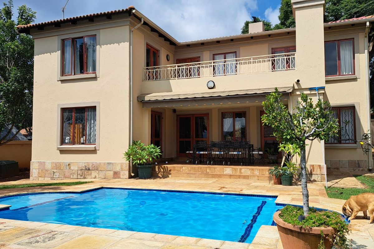 Rear view of a two-story house featuring a swimming pool, stone patio, and an upper-level balcony with a metal railing.