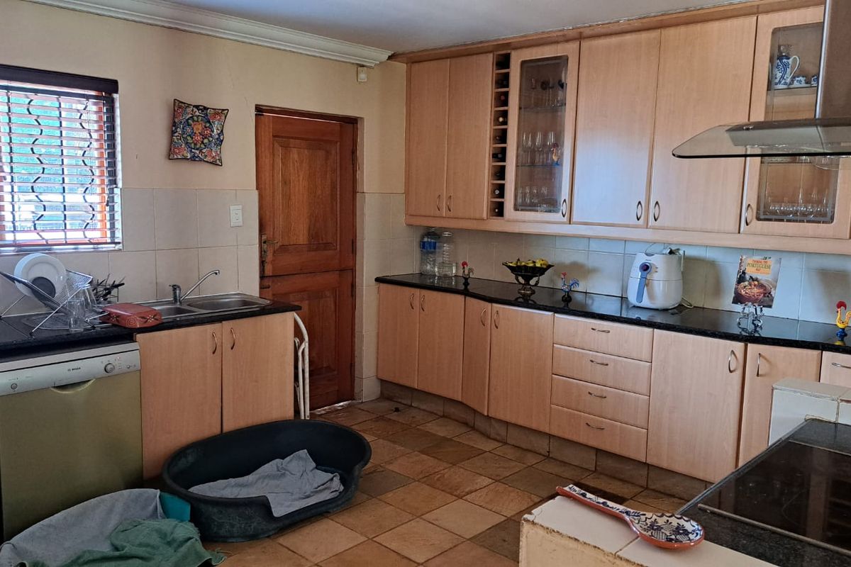 A functional kitchen featuring light wood laminate cabinetry, dark granite countertops, and tiled flooring, offering a practical layout with ample storage space.