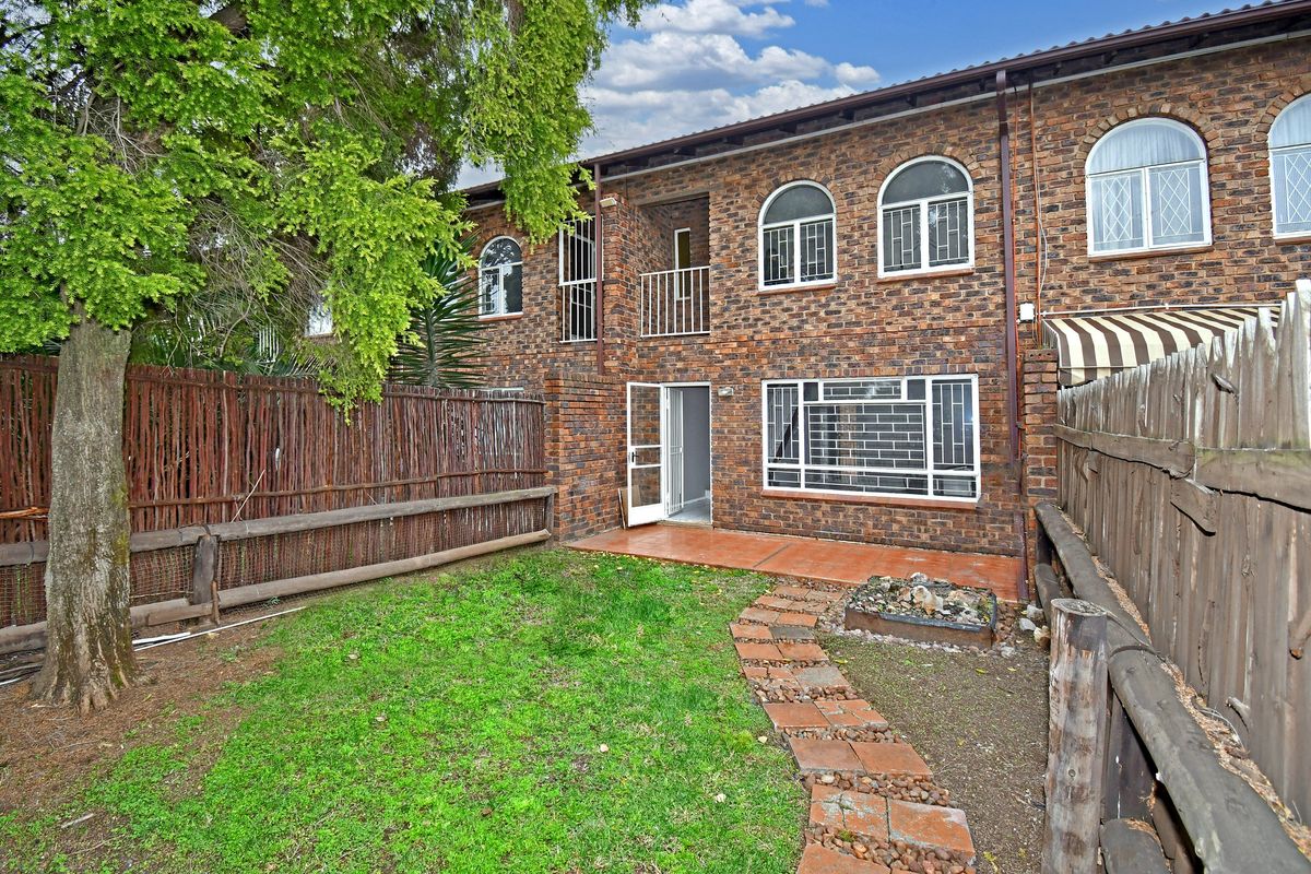 Rear view of a face brick townhouse featuring a private garden, tiled patio area, and secure arched windows.