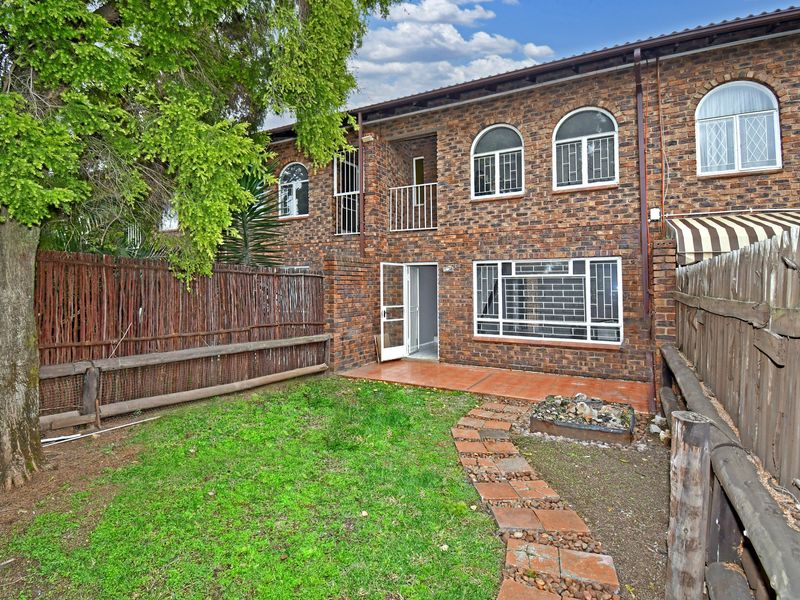 Rear view of a face brick townhouse featuring a private garden, tiled patio area, and secure arched windows.