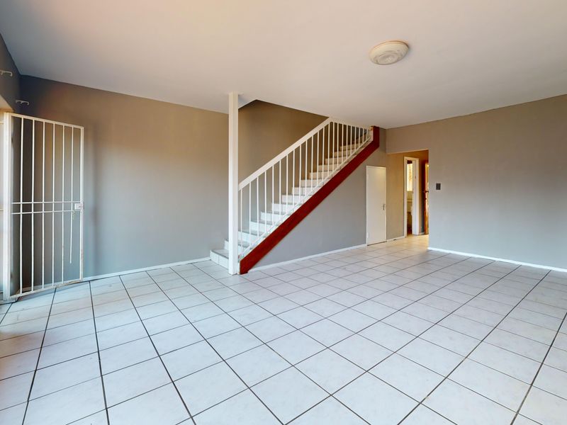 An open-plan living area featuring tiled flooring, a central staircase with a metal railing, and a security gate at the entrance.