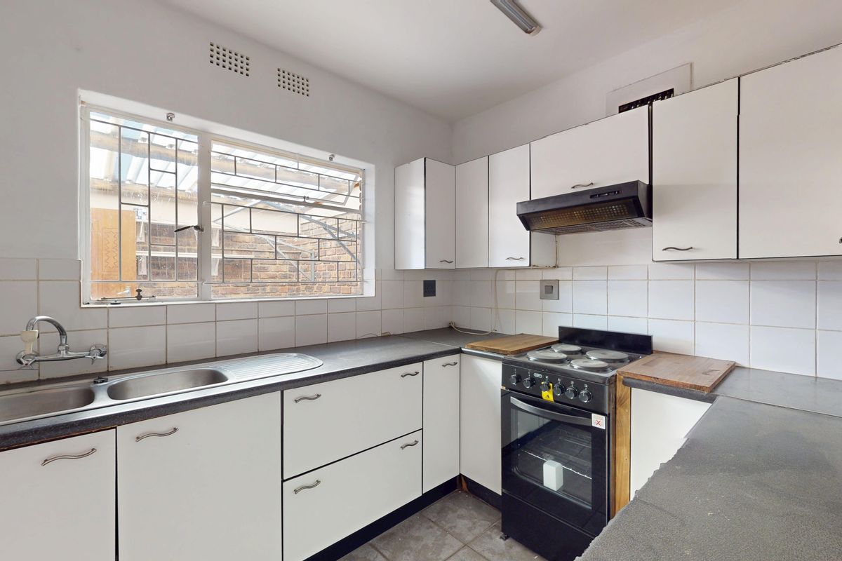 A functional kitchen featuring white cabinetry, a stainless steel sink, a tiled backsplash, and a freestanding stove, offering potential for modern updates.