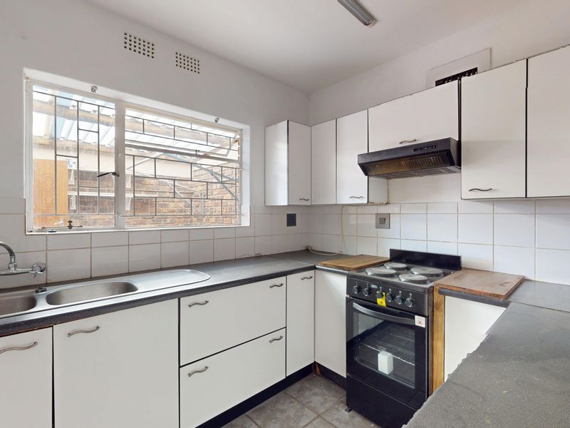 A functional kitchen featuring white cabinetry, a stainless steel sink, a tiled backsplash, and a freestanding stove, offering potential for modern updates.