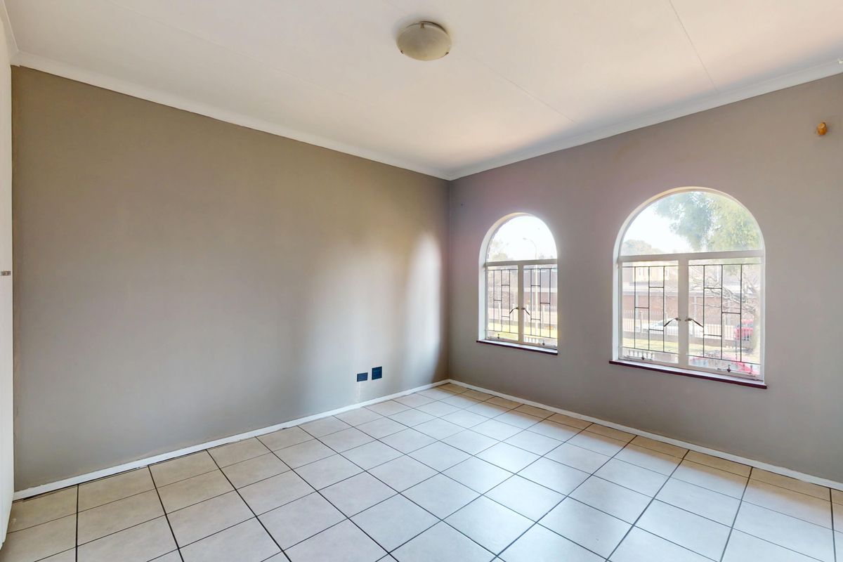 A bright, empty bedroom featuring neutral walls, tiled flooring, and two arched windows with security bars, offering a clean canvas for personalization.
