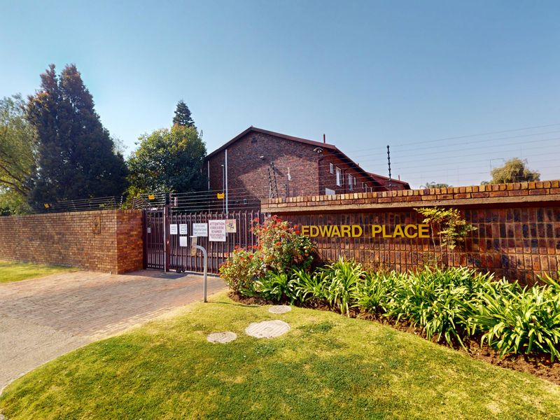 Front entrance view of Edward Place townhouse complex featuring a brick boundary wall, electric fencing, and a secure gated driveway entrance.