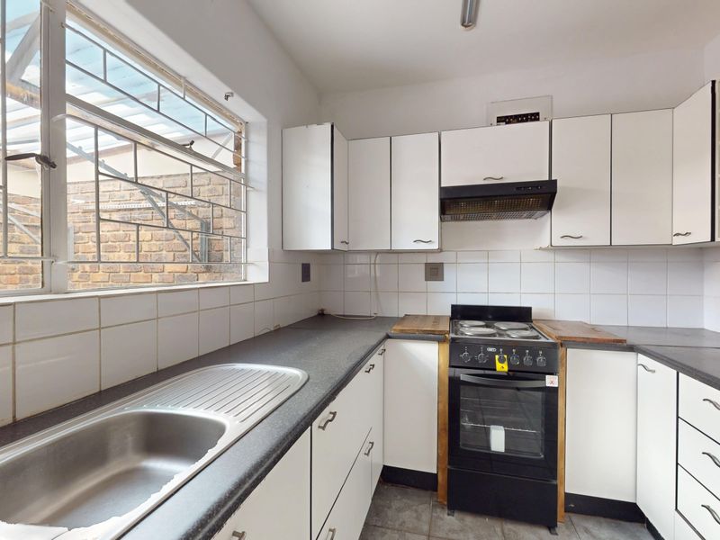 A functional kitchen featuring white cabinetry, dark laminate countertops, a stainless steel sink, and a freestanding stove with an extractor fan.