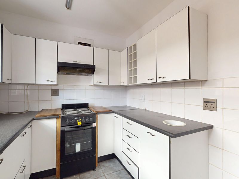 A functional kitchen featuring white cabinetry, dark laminate countertops, a tiled backsplash, and a freestanding stove with an extractor fan.