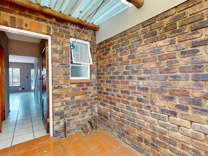 A functional utility or scullery area featuring exposed brick walls, tiled flooring, and direct access to the interior living space.