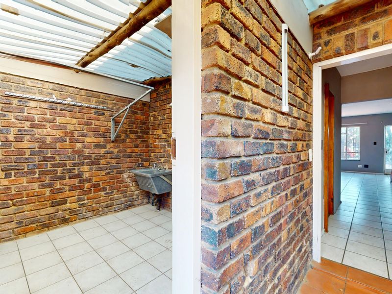 A functional laundry area featuring exposed brick walls, tiled flooring, and a utility sink, covered by a corrugated roof structure.