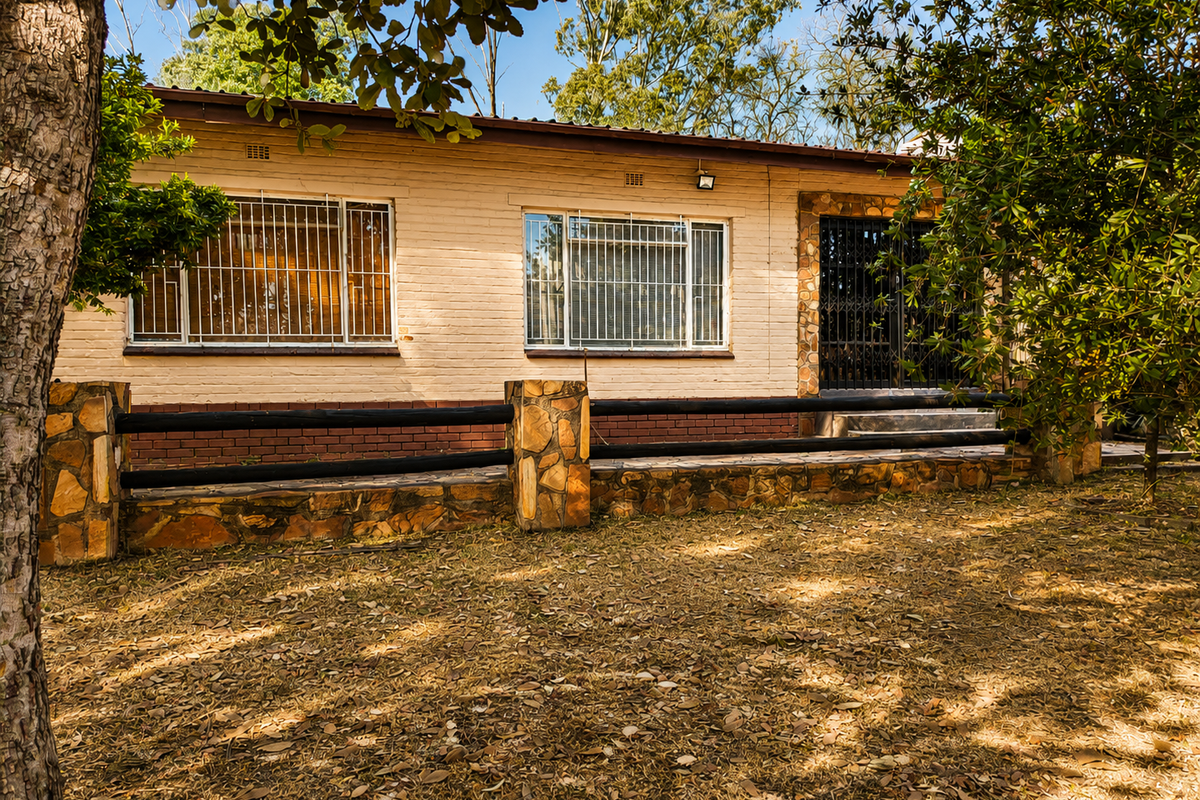 Rear view of a single-story brick house featuring stone-clad accents, security bars on windows, and a timber rail fence bordering the garden area.