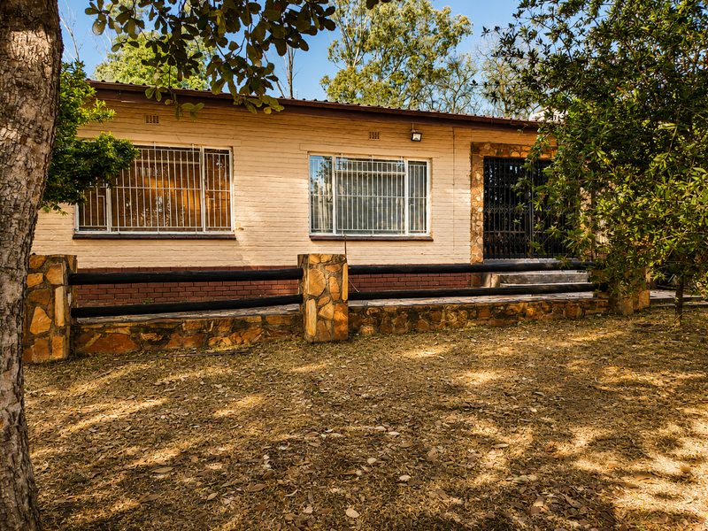 Rear view of a single-story brick house featuring stone-clad accents, security bars on windows, and a timber rail fence bordering the garden area.