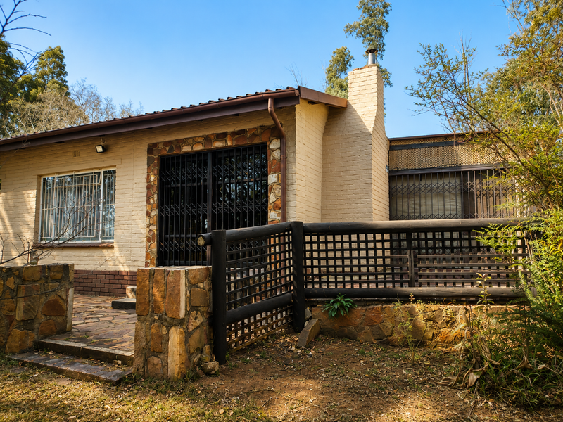 Rear exterior view of a single-story brick house featuring stone accents, a chimney, security gates, and a paved patio area with timber railing.