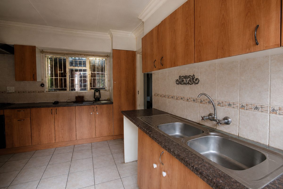 A functional kitchen featuring wood-look laminate cabinetry, double stainless steel sink, tiled splashbacks, and ceramic floor tiles, offering a clean and practical workspace.