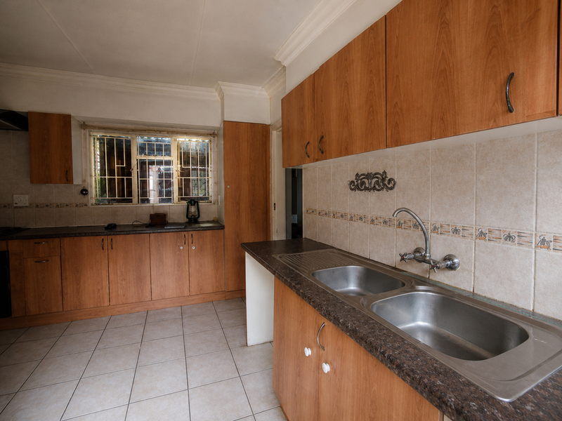 A functional kitchen featuring wood-look laminate cabinetry, double stainless steel sink, tiled splashbacks, and ceramic floor tiles, offering a clean and practical workspace.