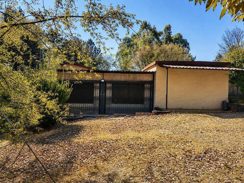 Rear view of the property featuring a brick facade, covered patio area, and metal security gates overlooking a garden space.
