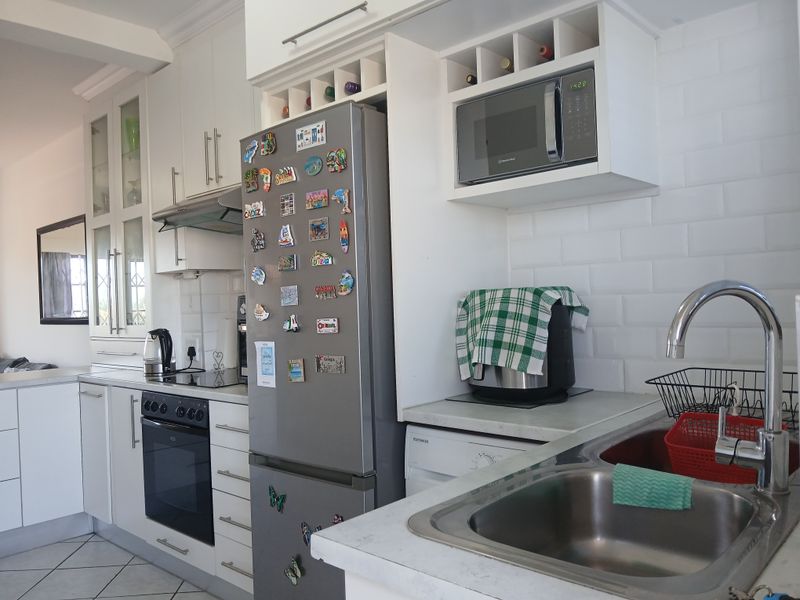 A functional kitchen featuring white cabinetry, subway tile backsplash, built-in oven, extractor fan, microwave, and a stainless steel sink with a modern mixer tap.