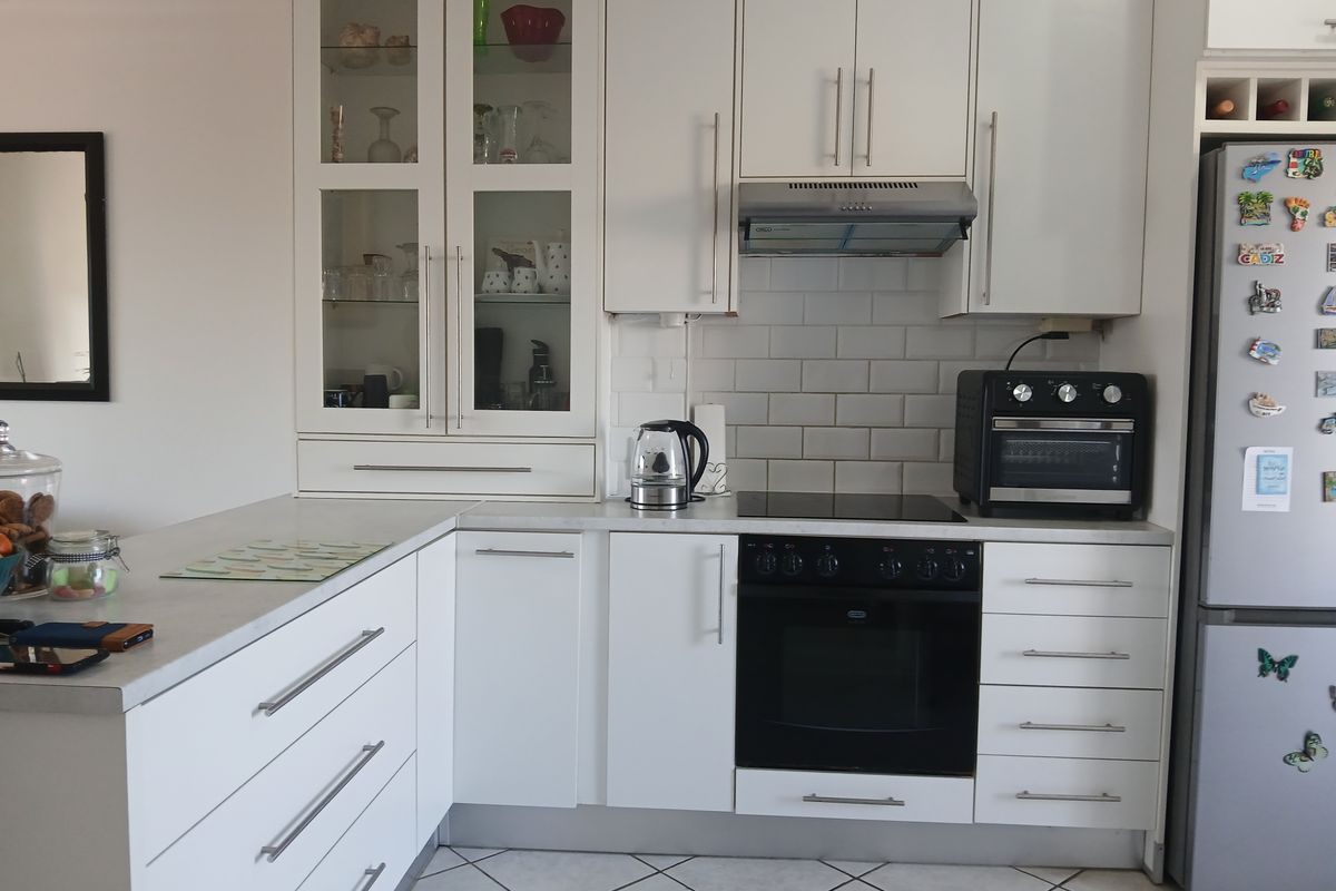 A well-maintained kitchen featuring white cabinetry, subway tile backsplash, integrated oven and cooktop, and glass-front display cabinets with tiled flooring.