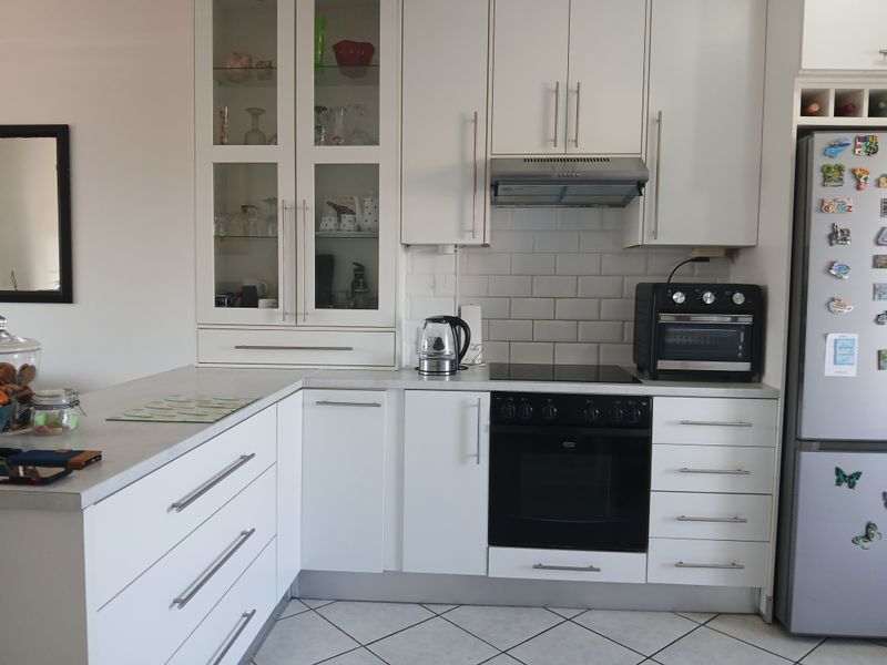 A well-maintained kitchen featuring white cabinetry, subway tile backsplash, integrated oven and cooktop, and glass-front display cabinets with tiled flooring.