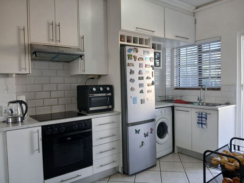 A functional kitchen featuring white cabinetry, subway tile backsplash, integrated oven and hob, and tiled flooring with a window providing natural light.