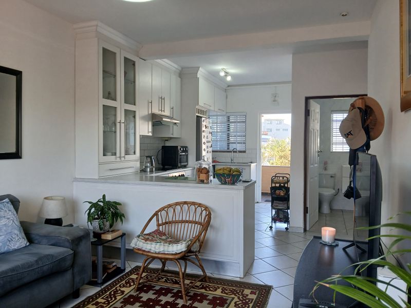 Open-plan living area featuring a functional kitchen with white cabinetry, tiled flooring, and direct access to a balcony and adjacent bathroom.