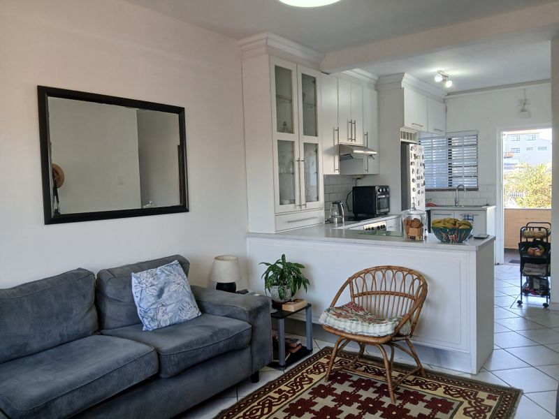 Open plan living area featuring a functional kitchen with white cabinetry, subway tile backsplash, and a breakfast counter, flowing into a comfortable lounge space.