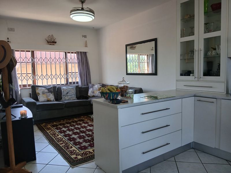 Open-plan living and kitchen area featuring white cabinetry, a kitchen island, tiled floors, and a window with security bars.