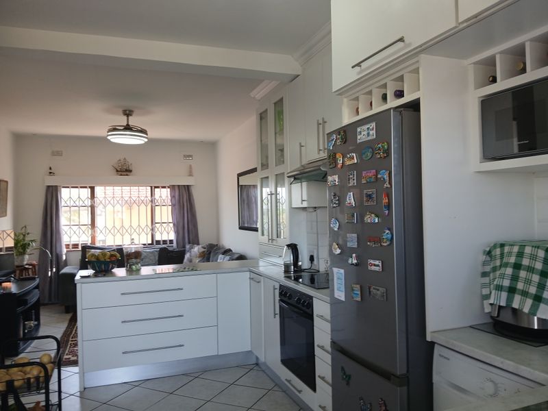 Open-plan kitchen and living area featuring white cabinetry, built-in appliances, tiled flooring, and a security gate on the window.