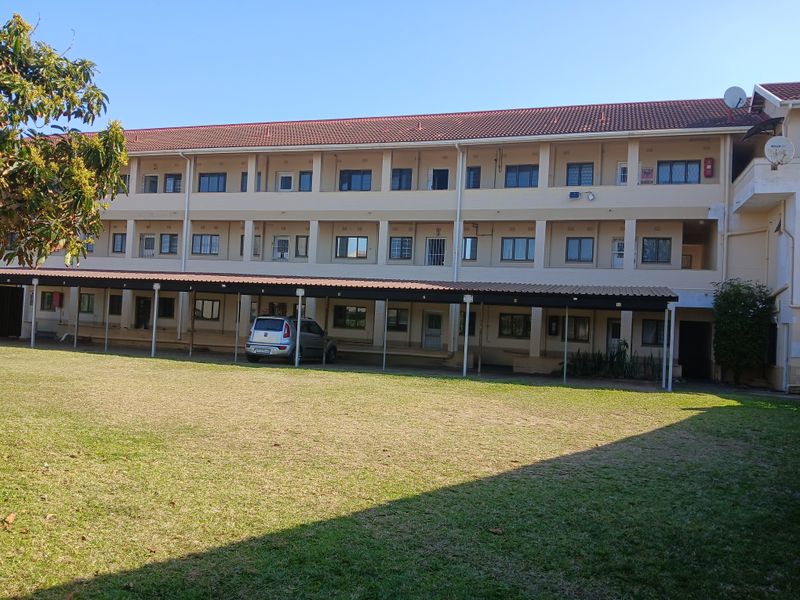 Rear view of a multi-story apartment complex featuring a large lawn area and covered parking bays for residents.