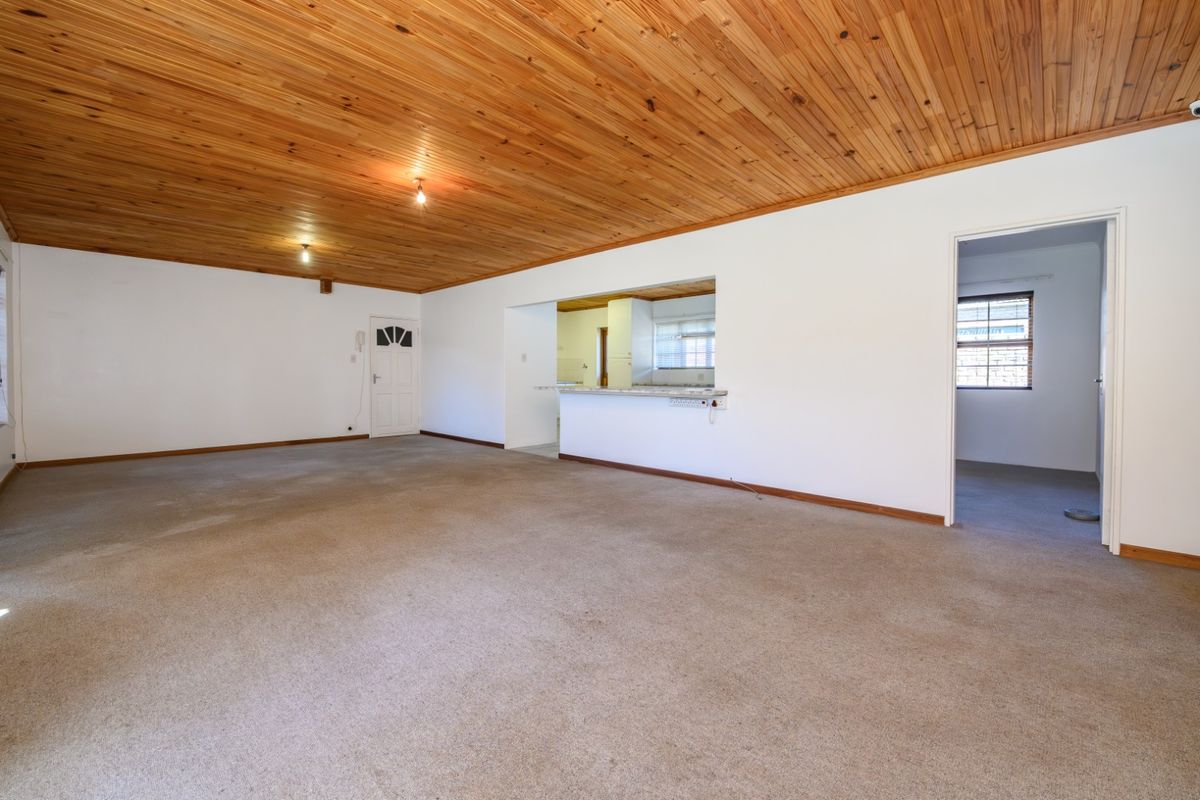 Spacious, empty living area featuring a timber tongue and groove ceiling, carpeted flooring, and a convenient pass-through window connecting to the kitchen.